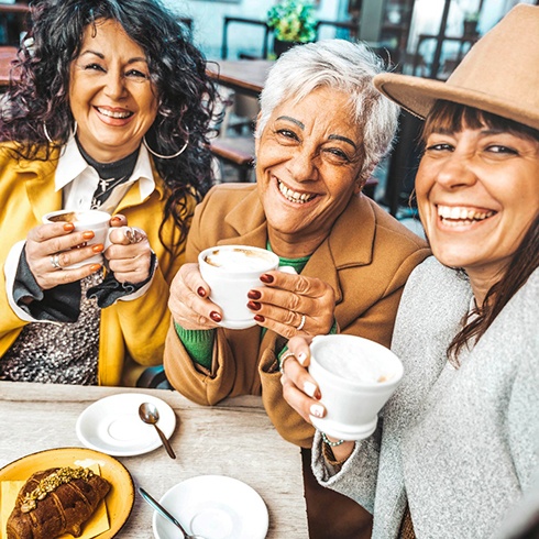 Three senior women smiling at table with coffee mugs
