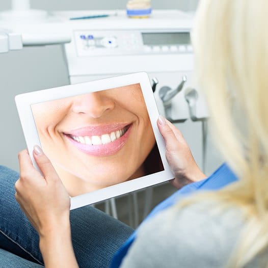 Woman looking at tablet screen showing flawless smile after cosmetic dentistry in Mineola