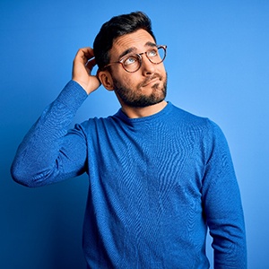 Confused man in blue sweater scratching his head