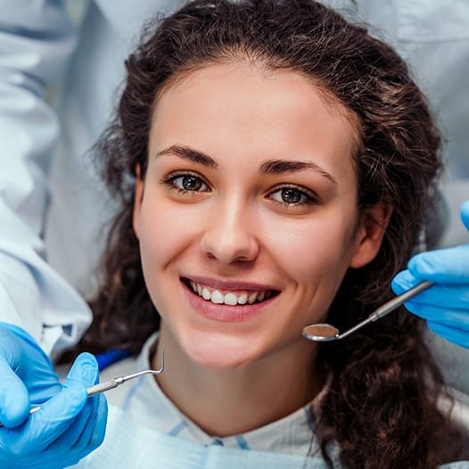 Woman with curly brown hair smiling in dental chair