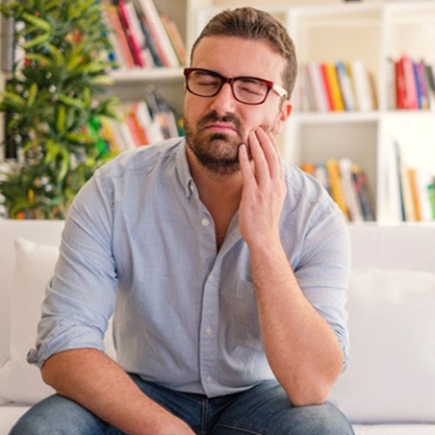 Man sitting on couch and holding his cheek in pain