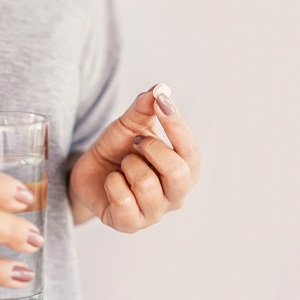 Person holding white pill and glass of water