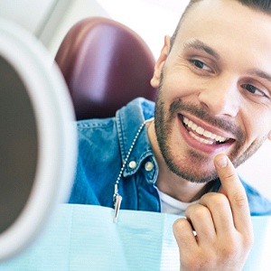 Man in dental chair pointing to his teeth and looking in mirror