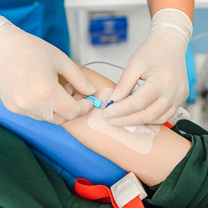 Person placing I V needle in the arm of a patient