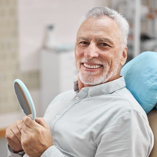 Smiling older man in dental chair holding a mirror