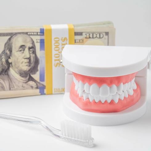 Model of teeth next to toothbrush and stack of hundred dollar bills