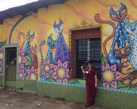 Dental team member posing for a picture with a cat mural