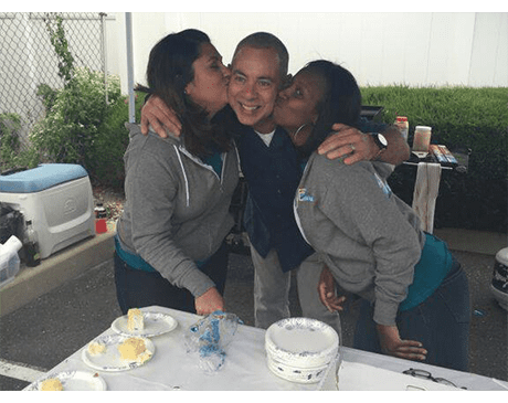 Two dental team members kissing dentist's cheek at community event