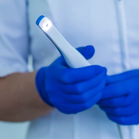 Gloved hands holding a white pen like intraoral camera