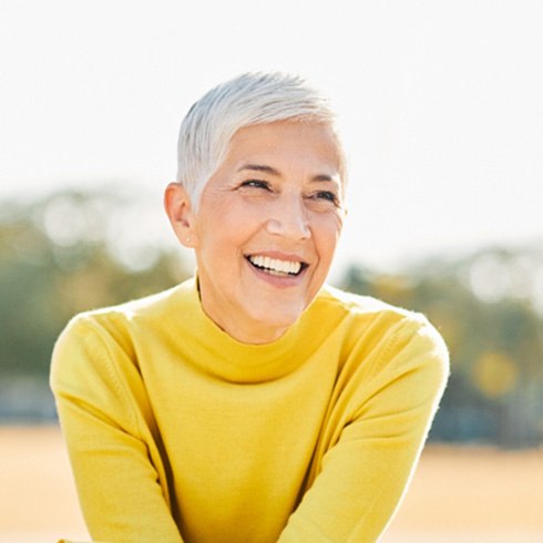 Senior woman in yellow shirt sitting outside and smiling