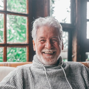 Senior man in grey sweater smiling and sitting in chair
