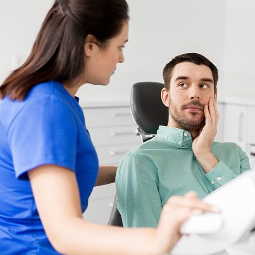 Man holding his cheek in pain while talking to emergency dentist