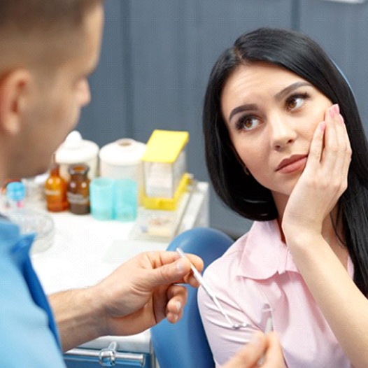 Woman holding her cheek in pain while talking to dentist about dental implant failure in Mineola