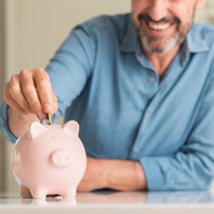 man putting coins into a pink piggy bank 