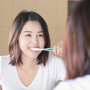 Young woman brushing her teeth in front of mirror