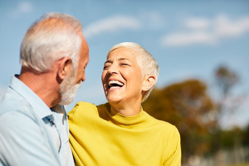 Older couple with dental implants smiling outside