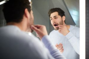 man with a knocked-out tooth looking at his mouth in a mirror