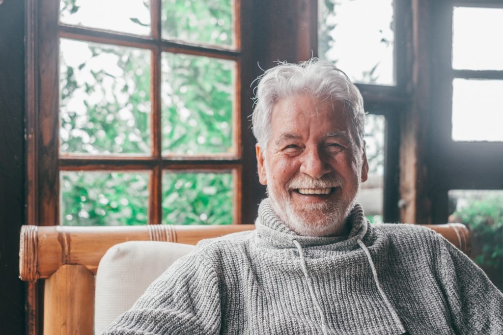 Closeup of senior man in grey sweater smiling at home
